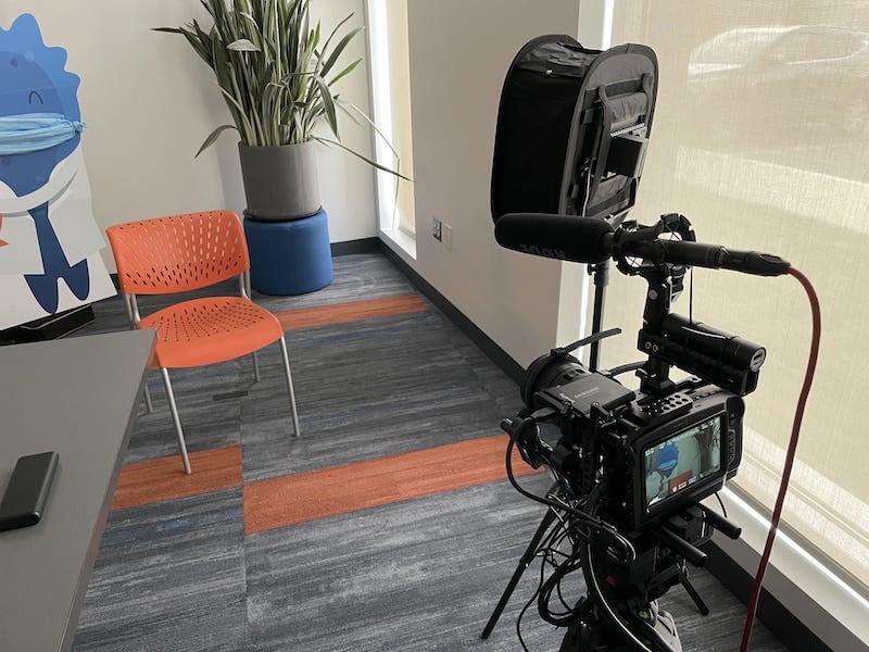 Camera set up with a chair in front of it and the Blugene mascot cutout wearing a mask in the back