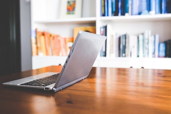 open laptop on a desk with a bookshelf in the background