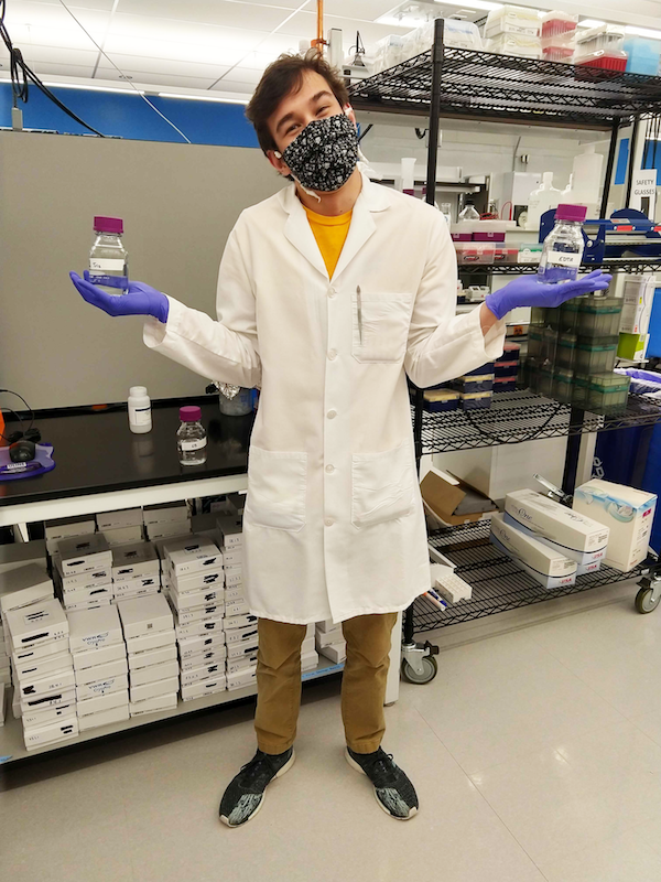 An Addgenie in the lab in a lab coat and mask holding up Tris buffer in one hand and TE buffer in the other hand