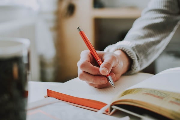 Close up image of a person writing in a notebook with an orange pen