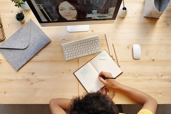 top view photo of person writing on white paper during a video meeting