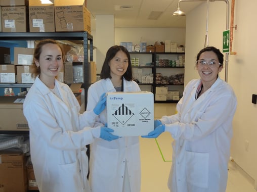 Three scientists in lab coats holding a box.