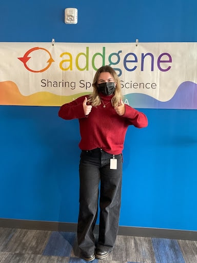 Woman posing with her thumbs up and smiling in front of an Addgene banner. 